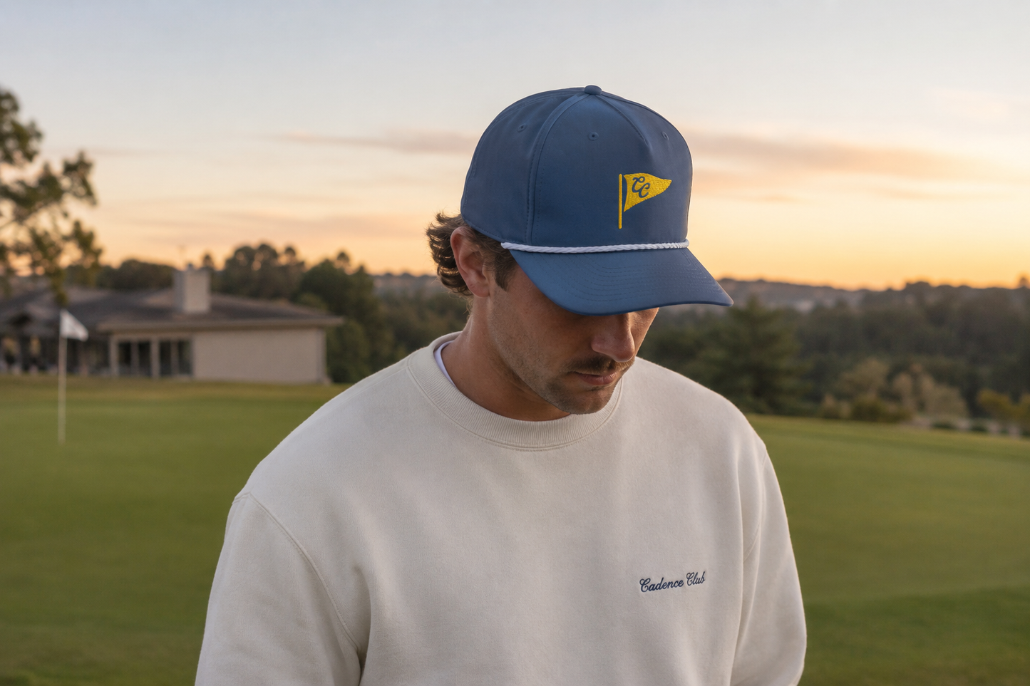 Man wearing a blue cap with a logo on a golf course at sunset
