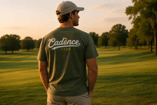 Man wearing a green 'Cadence Club' t-shirt standing on a golf course at sunset.